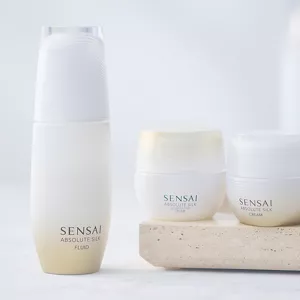 Absolute Silk Fluid on white surface next to wooden tray with complementary Step 2 creams